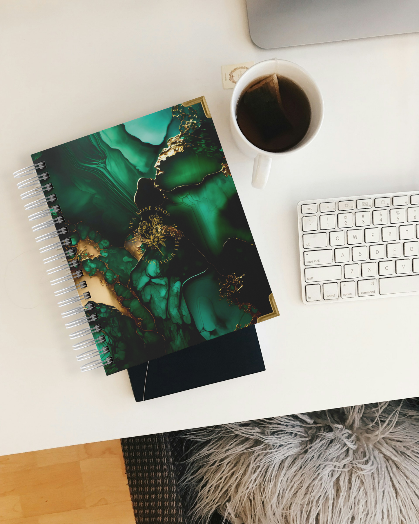 Planner, coffee cup, and keyboard on a desk with a laptop in the background