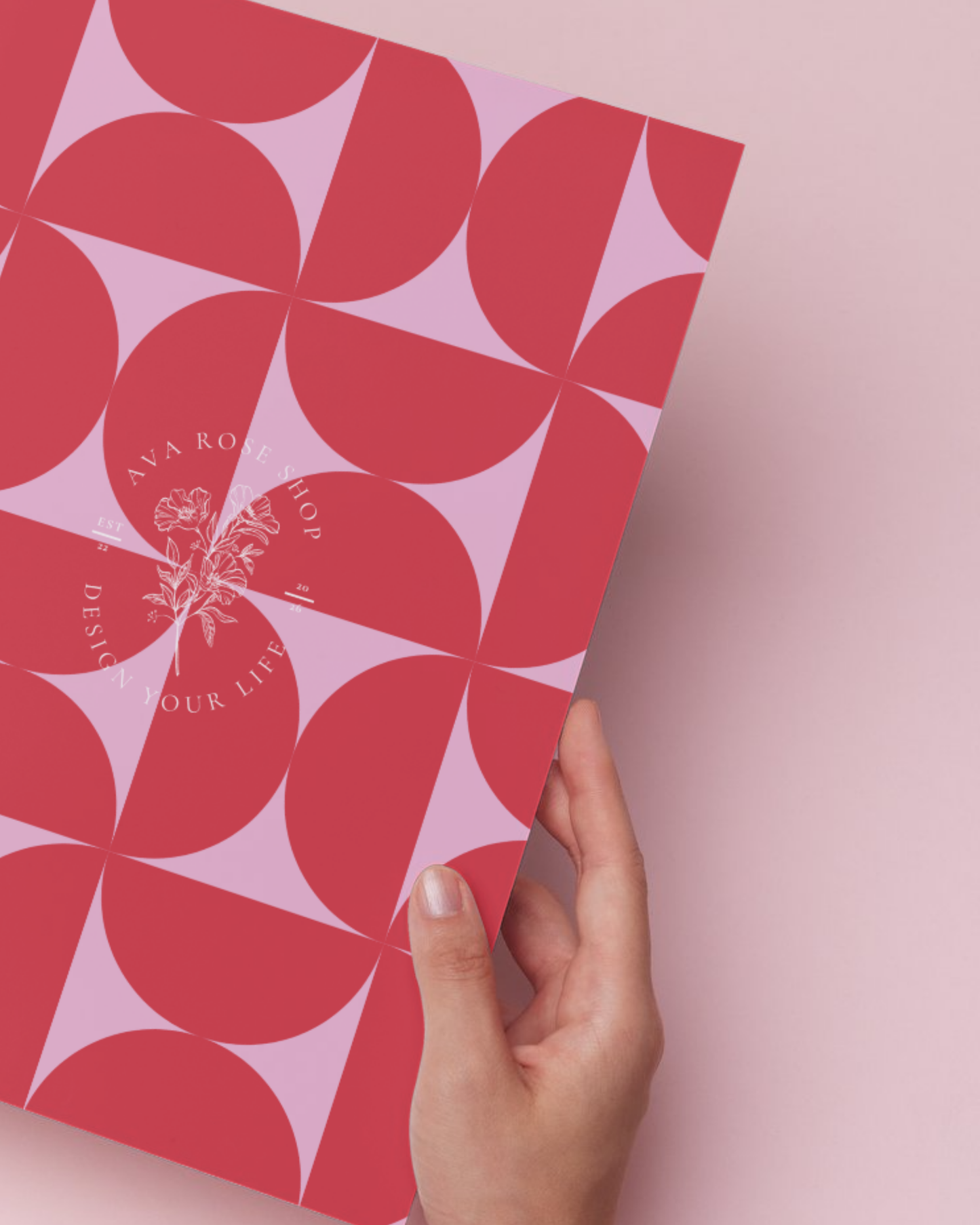 Hand holding a pink and red patterned planner against a pink background