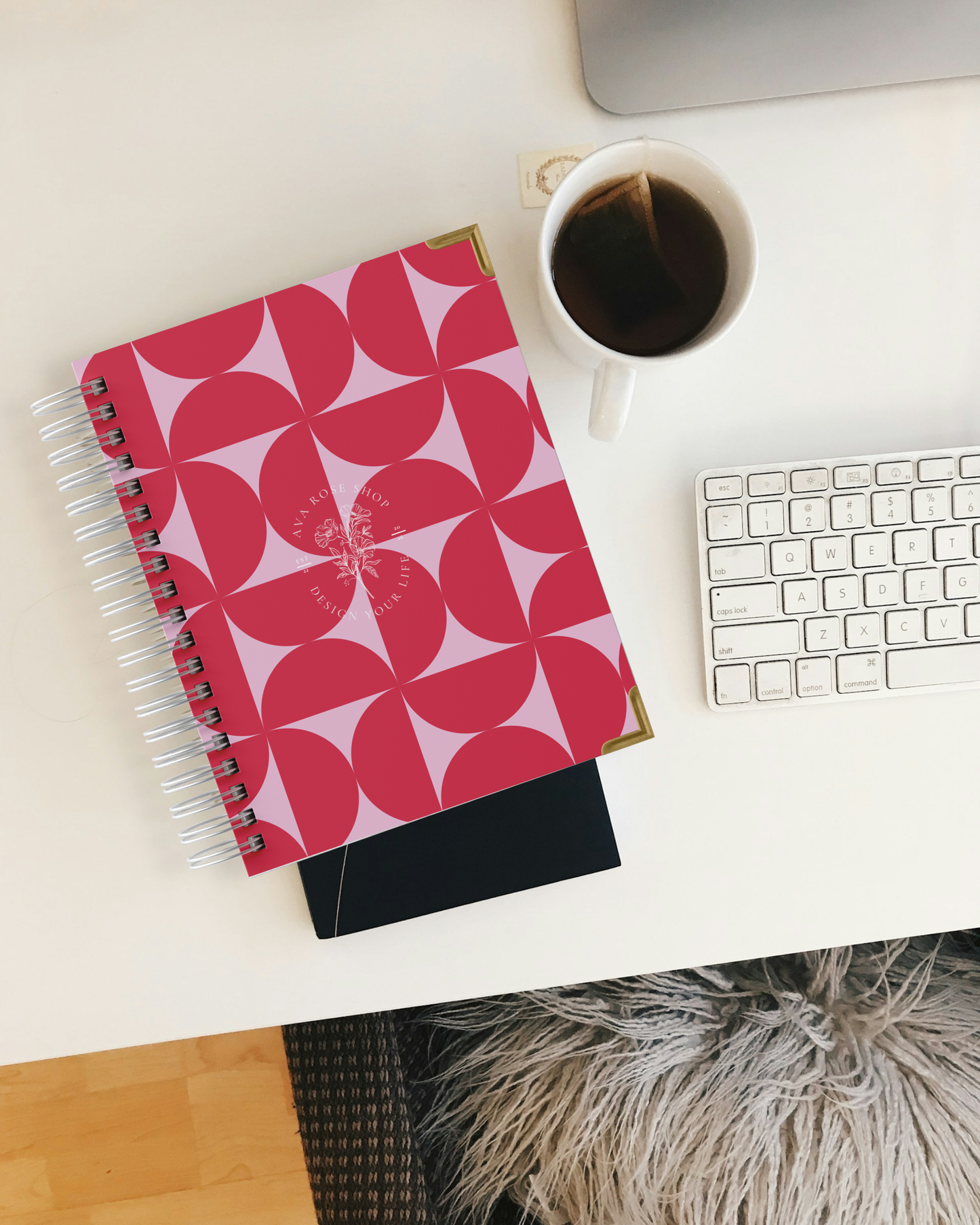 Pink geometric planner with a white cup of coffee and keyboard on a desk.