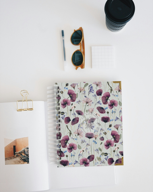 Floral planner with sunglasses, pen, and coffee cup on a white surface