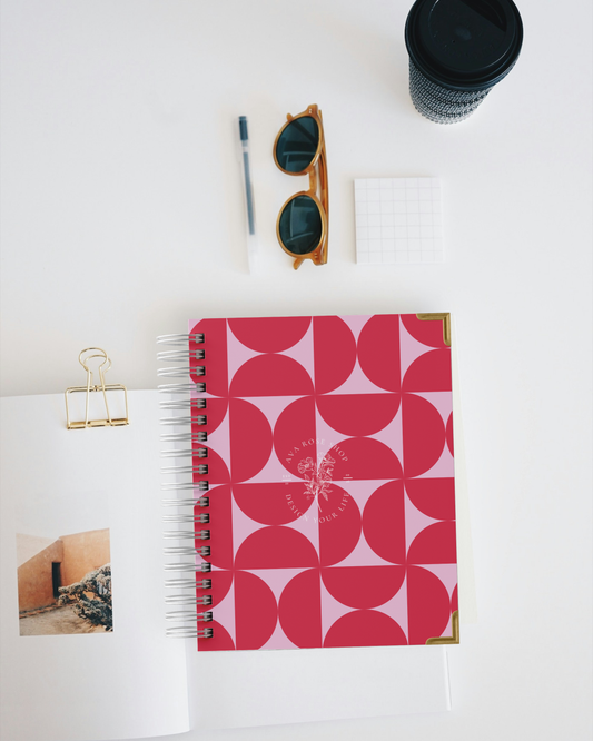 Pink geometric planner with sunglasses, pen, and photo on a white surface